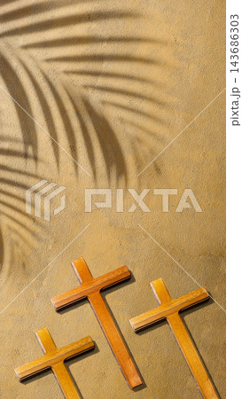 Three wooden crosses resting on sand with a palm frond shadow cast above, symbolizing the crucifixion and resurrection of Jesus Christ. Concept of Christian Three wooden crosses resting on sand with a palm frond shadow cast above, symbolizing the crucifixion and resurrection of Jesus Christ. Concept of Christian 143686303