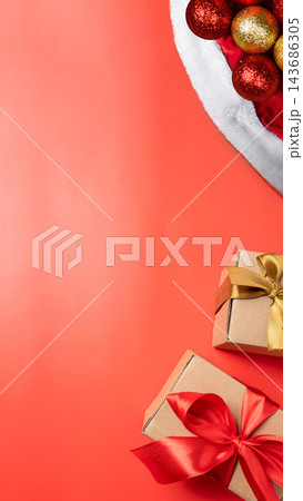Christmas background on coral orange surface with Santa hat, gold and red ornaments, and wrapped gift boxes with ribbons. Top view with copy space. Concept of Merry Christmas Christmas background on coral orange surface with Santa hat, gold and red ornaments, and wrapped gift boxes with ribbons. Top view with copy space. Concept of Merry Christmas 143686305