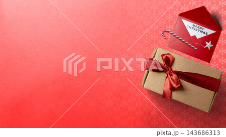 Christmas composition with a craft gift box tied with a red ribbon and an envelope with a Merry Christmas card on a red background. Concept of Merry Christmas 143686313