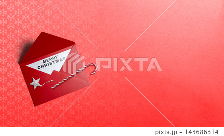 Red Christmas envelope with 'Merry Christmas' note, candy cane, and silver star on red textured background with copy space. Concept of Merry Christmas 143686314