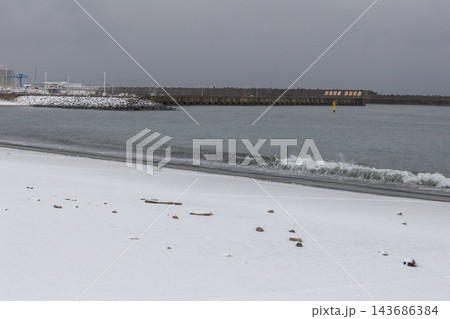 雪の積もった砂浜に打ち寄せる冬の波と防波堤 143686384