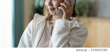 スマートフォンで通話しながら微笑む主婦の様子 スマートフォンで通話しながら微笑む主婦の様子 143687289