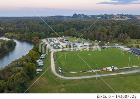 Aerial view of caravans at a campground beside the Brunswick River in Mullumbimby, with a sports field and forest under a hazy evening sky in northern New South Wales. Aerial view of caravans at a campground beside the Brunswick River in Mullumbimby, with a sports field and forest under a hazy evening sky in northern New South Wales. 143687328
