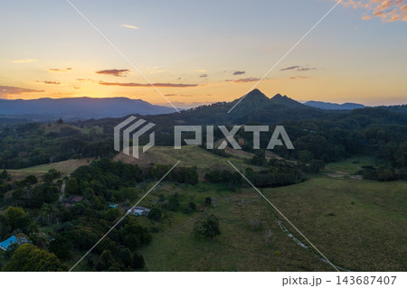 Aerial view of Mount Chincogans twin peaks above forest and farmland near Mullumbimby, with a warm sunset sky over the Northern Rivers in New South Wales. Aerial view of Mount Chincogans twin peaks above forest and farmland near Mullumbimby, with a warm sunset sky over the Northern Rivers in New South Wales. 143687407