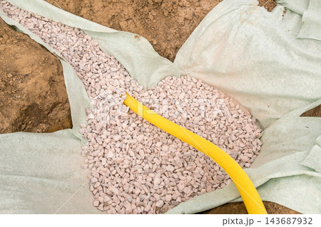 Granular stones being carefully placed over protective landscaping fabric and a yellow drainage pipe. 143687932