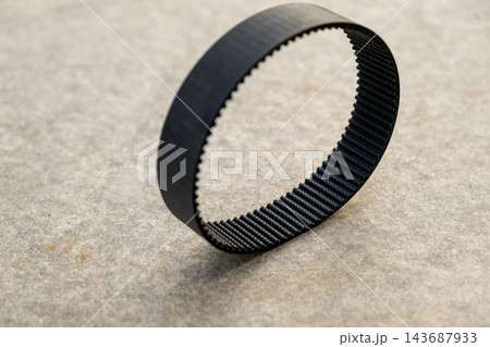 An industrial black rubber drive belt is laid out on a concrete surface, ready for machinery maintenance. The belt is flexible and designed for durable performance. 143687933