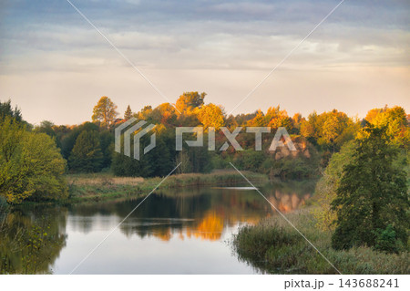 Golden Autumn Forest Landscape Reflected in Calm River Water During Peaceful October Sunset 143688241