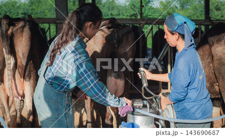 Two Asian female farmers cleaning and preparing automated milking equipment in livestock farm shed for fresh milk production. traditional agriculture business. hygiene and rural lifestyle background. 143690687