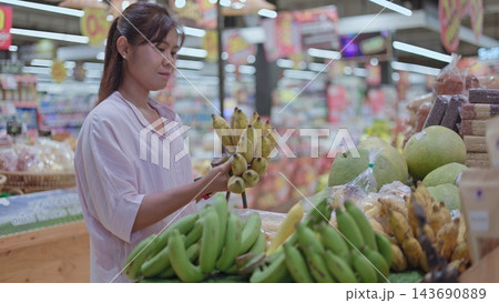 Asian Woman Choosing Fresh Bananas in Supermarket Grocery Store 143690889