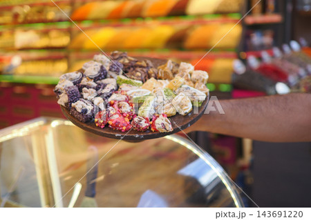 A person holds a plate of turkish delights in a shop filled with colorful treats 143691220
