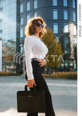 Attractive Businesswoman Standing In City With Black Bag Wearing White Shirt And Sunglasses. Corporate Fashion Lifestyle Concept Female Professional Urban Style Attractive Businesswoman Standing In City With Black Bag Wearing White Shirt And Sunglasses. Corporate Fashion Lifestyle Concept Female Professional Urban Style 143693064