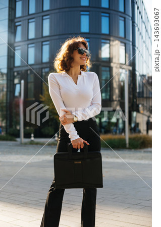 Attractive Businesswoman Standing In City Holding Black Handbag Wearing Elegant Outfit And Sunglasses. Corporate Fashion Lifestyle Concept Female Professional Attractive Businesswoman Standing In City Holding Black Handbag Wearing Elegant Outfit And Sunglasses. Corporate Fashion Lifestyle Concept Female Professional 143693067