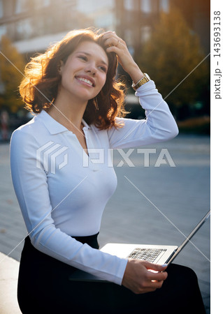 Beauty woman smiling while working on laptop outdoors. Beautiful woman presenting confident professional lifestyle with portable computer. Flexible career concept. 143693138