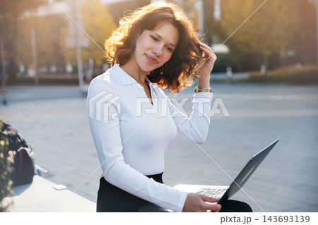Attractive woman using laptop with elegant professional appearance outdoors. Young woman embracing modern digital business lifestyle confidently. Mobile office concept. 143693139