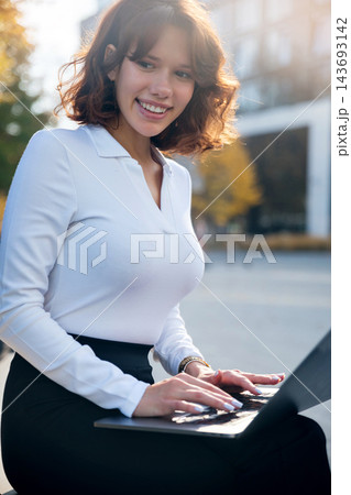 Young woman smiling while using laptop outdoors confidently. Beautiful woman embracing modern digital business lifestyle. Online work concept. Young woman smiling while using laptop outdoors confidently. Beautiful woman embracing modern digital business lifestyle. Online work concept. 143693142