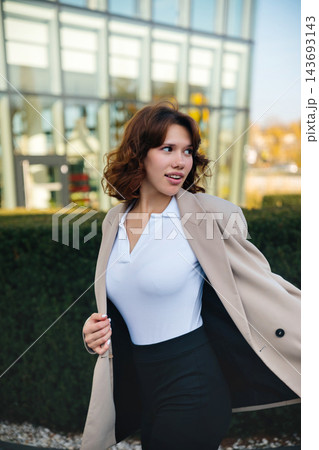 Beautiful woman adjusting elegant blazer with confident business appearance. Attractive woman standing near modern office building outdoors. Corporate fashion concept. Beautiful woman adjusting elegant blazer with confident business appearance. Attractive woman standing near modern office building outdoors. Corporate fashion concept. 143693143