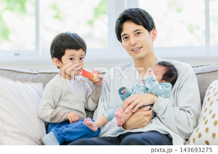 ソファーで赤ちゃんを抱っこするお父さんと男の子 ソファーで赤ちゃんを抱っこするお父さんと男の子 143693275