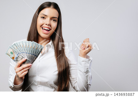 Woman smiles while holding cash and showing excitement in a studio setting 143693887