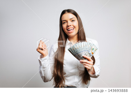 Woman smiles and holds cash in hands while standing in a bright indoor space during the day 143693888