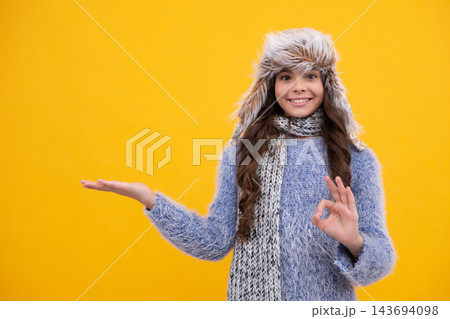 Teenager girl with winter hat over isolated yellow background. Winter christmas holidays, new year mood. Kids warm clothes. Happy face, positive and smiling emotions of teenager girl. Teenager girl with winter hat over isolated yellow background. Winter christmas holidays, new year mood. Kids warm clothes. Happy face, positive and smiling emotions of teenager girl. 143694098