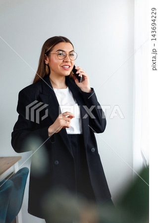 Attractive Business Woman Talking on Smartphone and Presenting Idea in Office. Corporate Workplace and Consulting Concept Attractive Business Woman Talking on Smartphone and Presenting Idea in Office. Corporate Workplace and Consulting Concept 143694229