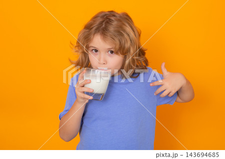 Organic milk. Child with a glass of milk on studio background. Cute boy in white shirt holding glass of milk on isolated on yellow. Portrait of kid with milk mustache. Organic milk. Child with a glass of milk on studio background. Cute boy in white shirt holding glass of milk on isolated on yellow. Portrait of kid with milk mustache. 143694685