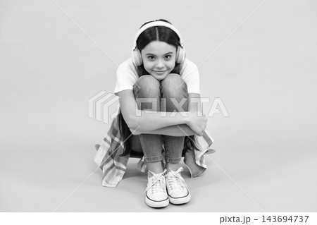 Teen girl in headphones listen to music. Wireless headset device accessory. Child enjoys the music in earphones on yellow background. Happy casual teenager. Urban kids style, stylish hipster teen. Teen girl in headphones listen to music. Wireless headset device accessory. Child enjoys the music in earphones on yellow background. Happy casual teenager. Urban kids style, stylish hipster teen. 143694737