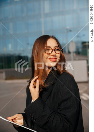 Pretty Business Woman Holding Tablet And Touching Hair Near Modern Office Building Wearing Black Blazer And Glasses. Corporate Lifestyle Concept Female Professional Pretty Business Woman Holding Tablet And Touching Hair Near Modern Office Building Wearing Black Blazer And Glasses. Corporate Lifestyle Concept Female Professional 143694940