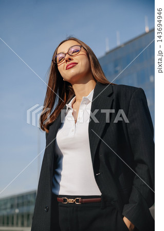 Beautiful Business Woman Portrait Looking Up Near Modern Office Building Wearing Black Suit And White Shirt. Corporate Lifestyle Concept Female Professional Urban Beautiful Business Woman Portrait Looking Up Near Modern Office Building Wearing Black Suit And White Shirt. Corporate Lifestyle Concept Female Professional Urban 143694946