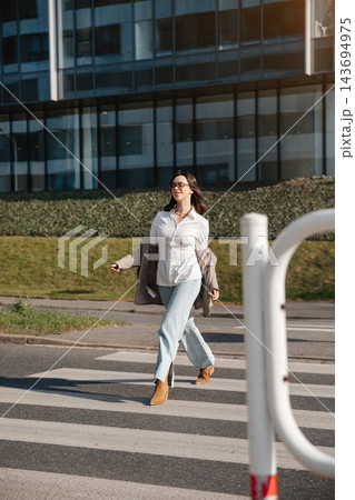 Beautiful Woman Walking Across Street Near Modern Office Building Wearing Beige Blazer And Jeans. Casual Business Lifestyle Concept Female Urban Beautiful Woman Walking Across Street Near Modern Office Building Wearing Beige Blazer And Jeans. Casual Business Lifestyle Concept Female Urban 143694975