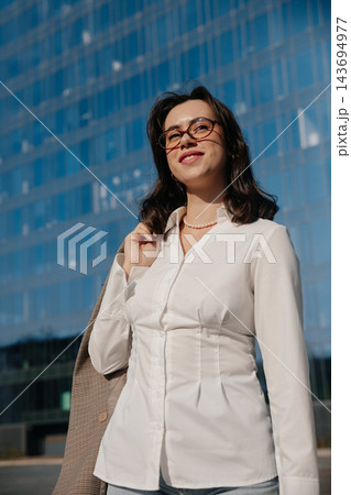 Beautiful Woman In White Shirt And Glasses Holding Blazer Near Modern Office Building. Casual Business Lifestyle Concept Female Urban Style 143694977