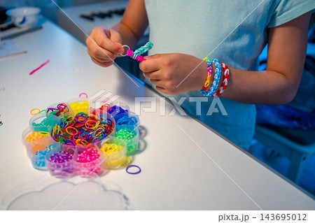 Child makes a bracelet from colorful rubber bands using a mini loom at home. Creative activity helps develop fine motor skills, hand eye coordination and concentration through play Child makes a bracelet from colorful rubber bands using a mini loom at home. Creative activity helps develop fine motor skills, hand eye coordination and concentration through play 143695012