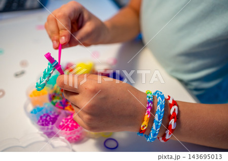 Child weaves a colorful bracelet from rubber bands using fingers and a crochet hook. Creative hobby develops fine motor skills, hand eye coordination and concentration through practice Child weaves a colorful bracelet from rubber bands using fingers and a crochet hook. Creative hobby develops fine motor skills, hand eye coordination and concentration through practice 143695013