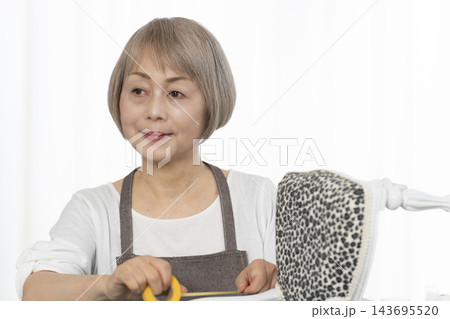 リビングで趣味のDIYでドールチェアーをリメイクするシニア女性 リビングで趣味のDIYでドールチェアーをリメイクするシニア女性 143695520