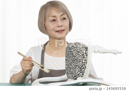 リビングで趣味のDIYでドールチェアーをリメイクするシニア女性 リビングで趣味のDIYでドールチェアーをリメイクするシニア女性 143695539
