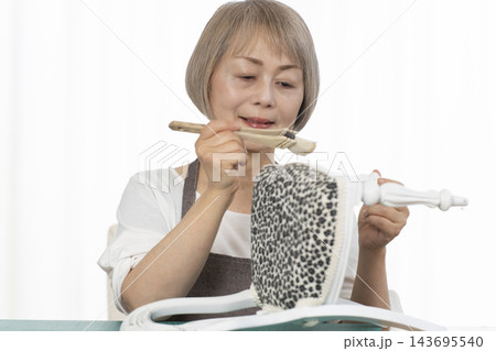 リビングで趣味のDIYでドールチェアーをリメイクするシニア女性 143695540