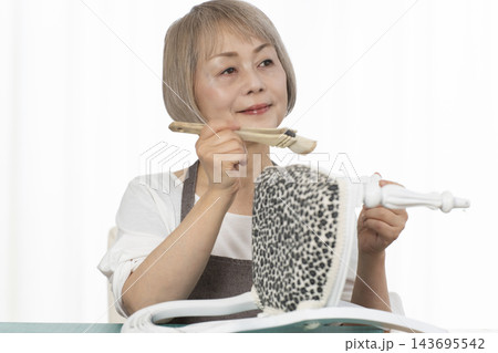 リビングで趣味のDIYでドールチェアーをリメイクするシニア女性 リビングで趣味のDIYでドールチェアーをリメイクするシニア女性 143695542