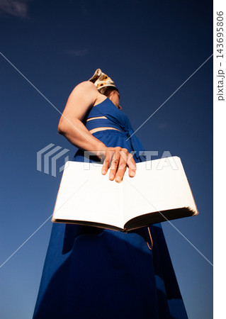 Woman in bright blue dress holding book in hands at very low angle against blue sky. Vertical image. Book lovers day 9 august Woman in bright blue dress holding book in hands at very low angle against blue sky. Vertical image. Book lovers day 9 august 143695806