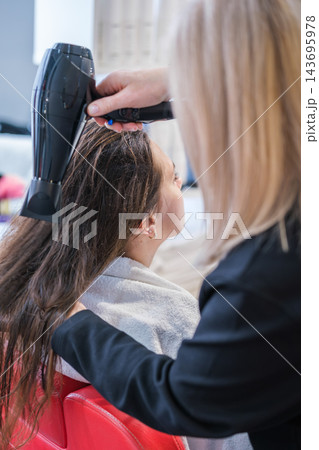 The beauty salon setting highlights a hairdresser, long hair, blow drying, a hair dryer, a female client, and a keratin treatment 143695978