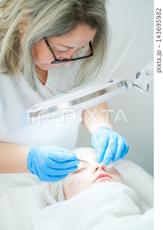 A beauty salon appointment centers on deep pore cleansing, an esthetician, magnifying lamp, manual extraction, a client, and facial cleansing 143695982