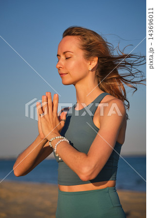With eyes closed, a woman holds the yoga Prayer Gesture, Namaskar Mudra, at her chest in a side portrait against the open blue sky 143696011
