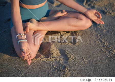 Viewed from above, the hands of a woman form Chin Mudra, the Consciousness Seal, on her knees during Padmasana yoga, Lotus Pose, while sitting on beach sand Viewed from above, the hands of a woman form Chin Mudra, the Consciousness Seal, on her knees during Padmasana yoga, Lotus Pose, while sitting on beach sand 143696014