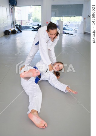 A female martial artist finishes ko-uchi-gari with an inside ankle reap, keeping a firm gi grip as her training partner lands backward on the tatami 143696021