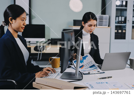 Two Asian businesswomen discussing work while walking outside a modern office building, one holding a digital tablet 143697761