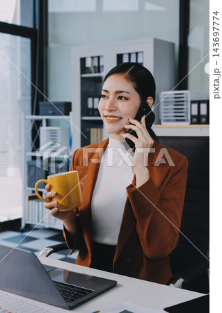 Two Asian businesswomen discussing work while walking outside a modern office building, one holding a digital tablet 143697774