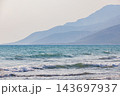 A tranquil seaside scene featuring gentle waves and distant mountains 143697937