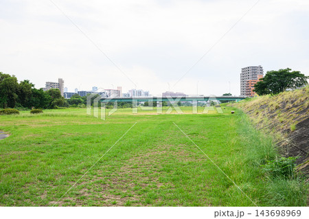 広い草地の向こうに橋梁と集合住宅が並ぶ都市郊外の緑地と明るい曇り空を撮影した風景写真素材 143698969