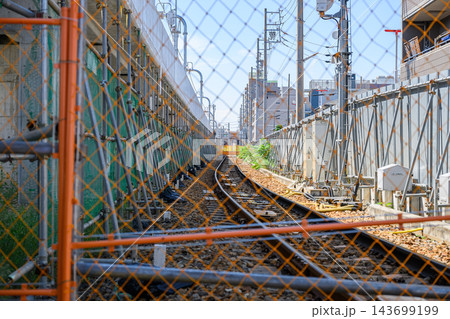 オレンジ色の金網フェンス越しに見える鉄道線路と電柱、工事用足場を正面から撮影した都市インフラの写真素 143699199