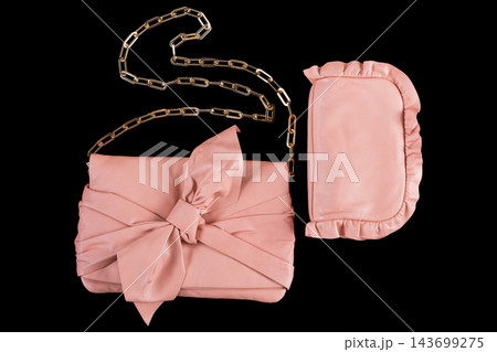 Pink leather womens clutch bag with bow and chain strap isolated on black background Pink leather womens clutch bag with bow and chain strap isolated on black background 143699275