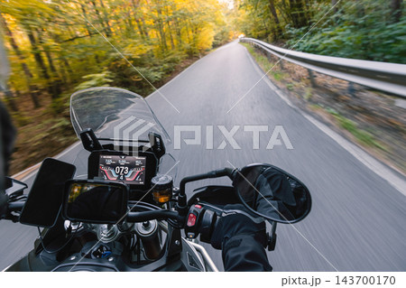 First person POV photograph from a moving motorcycle showing the handlebars, digital dashboard, mirrors and rider's gloved hand while traveling along an asphalt road through a green and golden autumn First person POV photograph from a moving motorcycle showing the handlebars, digital dashboard, mirrors and rider's gloved hand while traveling along an asphalt road through a green and golden autumn 143700170